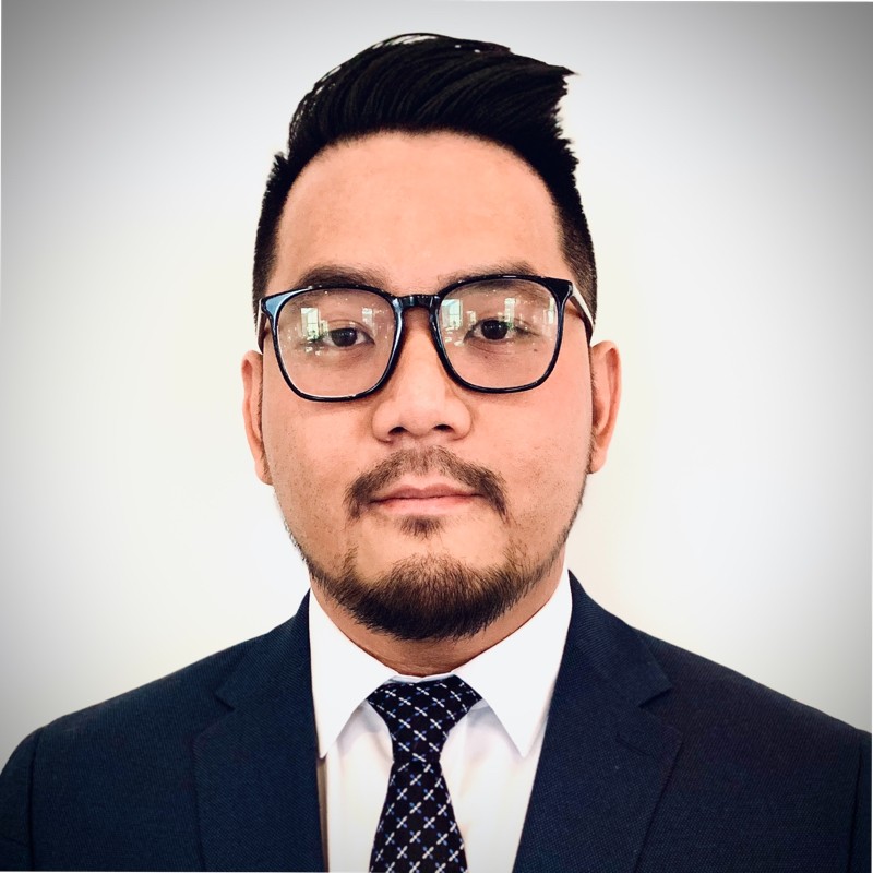 A professional headshot of a man with glasses, wearing a suit and tie, against a white background.