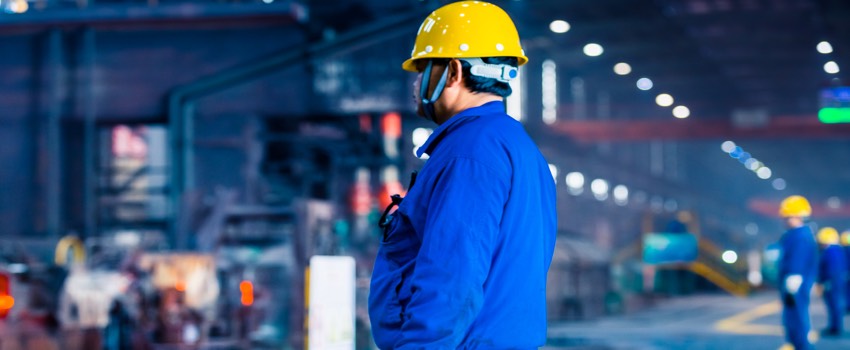 A worker in a blue uniform and hard hat oversees machinery, symbolically reflecting SysAid's Service Desk precision in ITSM. - SysAid