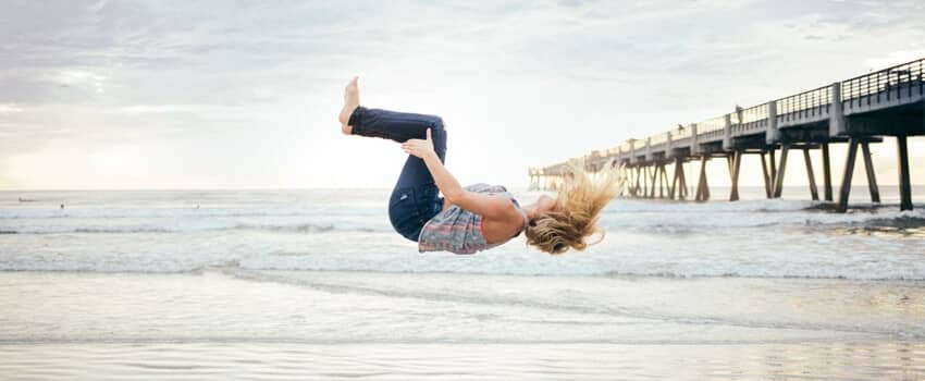 An agile individual performs a backflip on a beach, embodying the adaptability of SysAid's ITSM solutions in dynamic environments. - SysAid