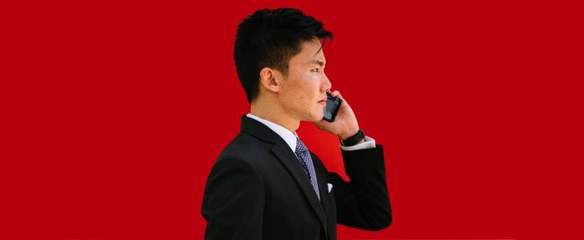 Person in suit on phone against red background, ready to tackle IT help desk inquiries with SysAid's efficient ITSM solutions. - SysAid