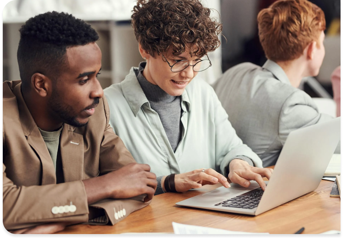 Three colleagues collaborate at a table using a laptop, streamlining workflows with SysAid ITSM solutions. - SysAid