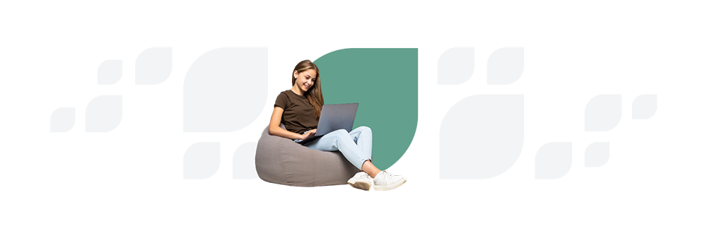 A woman sitting on a bean bag, smiling while using a laptop, against a white and green abstract background.