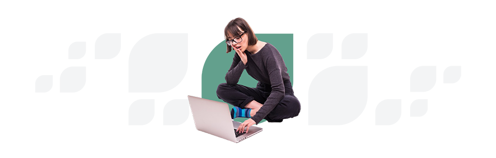 Young woman with glasses sitting on a transparent block, using a laptop, dressed in a black top and jeans, looking thoughtfully at the screen.