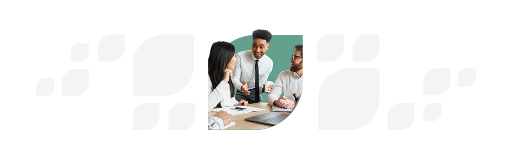 A group of three people in business attire engage in a lively discussion at a meeting table, with a laptop and documents in front of them. - SysAid