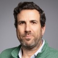 A man with short, dark hair and a trimmed beard wearing a green sweater poses against a plain grey background. - SysAid
