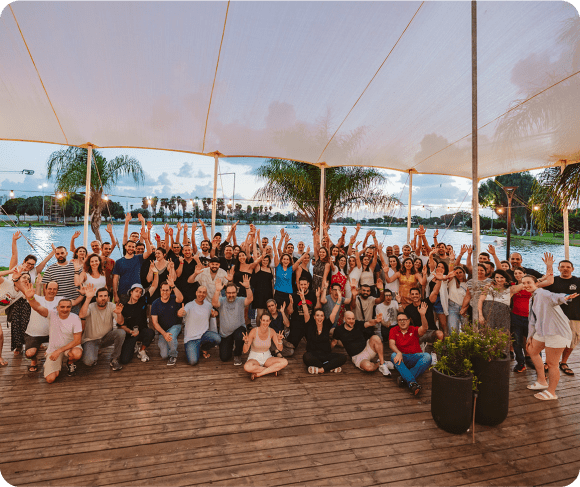 SysAid team celebrates success by the water, showcasing collaboration in ITSM under a bright canopy outdoors. - SysAid